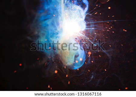 Arc welding. Welding of two sheets of metal by electrode in inert gases. Type MMA. A bright flash of light and a sheaf of sparks in a cloud of smoke. Miniature Universe. Free space for inscriptions. 