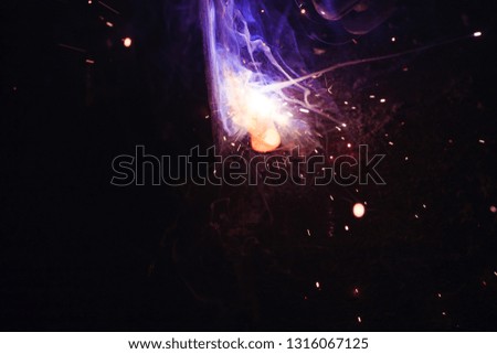 Arc welding. Welding of two sheets of metal by electrode in inert gases. Type MMA. A bright flash of light and a sheaf of sparks in a cloud of smoke. Miniature Universe. Free space for inscriptions. 