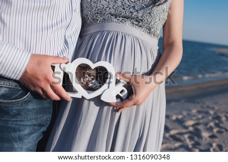 Future mother hugs her tummy by the sea. The family is expecting their child. Dad keeps a picture of the uzi.
