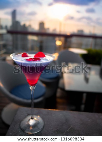 Red and purple colours valentine's day  or summer cocktail garnish with rose and sunset background at the roof top in Bangkok Thailand Royalty-Free Stock Photo #1316098304