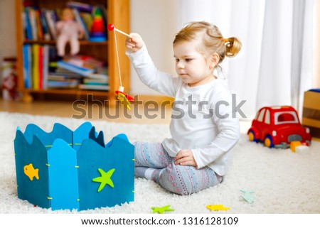 Adorable cute toddler girl playing with wooden fishing game at home or nursery. Happy healthy child training memory grabing with fishing rod . Development and coordination step and education of kid.