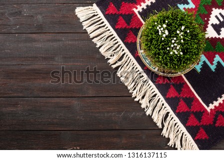 Novruz Green wheat grass semeni or sabzi in Azerbaijan, Persian new year on oriental motives pattern rug on wooden dark brown background. National folk carpet with white tassels, copy space