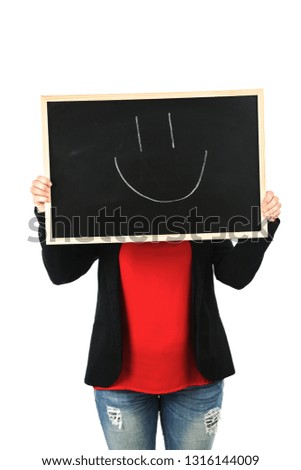 Young female teacher covering her face with a blackboard with a smiley face on it against a white background
