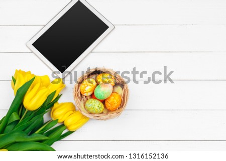 tablet screen for message and colorful tulips and easter eggs on wooden background
