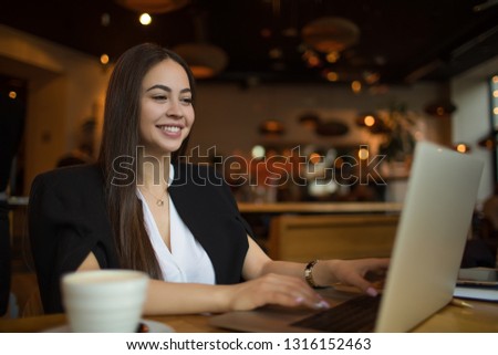 Happy smiling woman entrepreneur received good news in e-mail on laptop computer during coffee break in restaurant. Joyful female with good mood having conference via notebook, sitting in cafe 