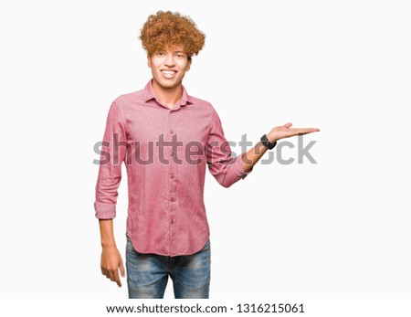 Young handsome business man with afro hair smiling cheerful presenting and pointing with palm of hand looking at the camera.