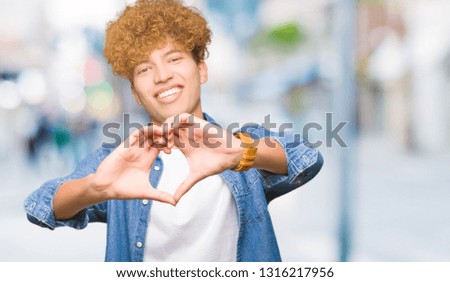 Young handsome man with afro hair wearing denim jacket smiling in love showing heart symbol and shape with hands. Romantic concept.