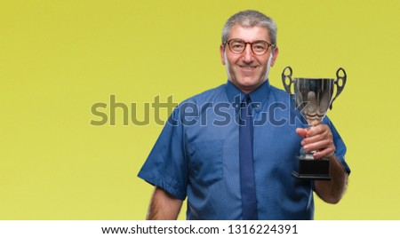 Handsome senior successful man holding trophy over isolated background with a happy face standing and smiling with a confident smile showing teeth
