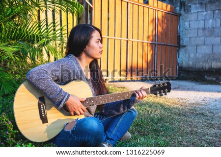 Young hipster woman playing a guitar in garden