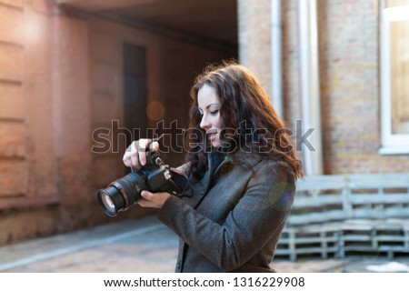 Girl in a coat on the street taking pictures holding a camera in her hands. Tourism in the city
