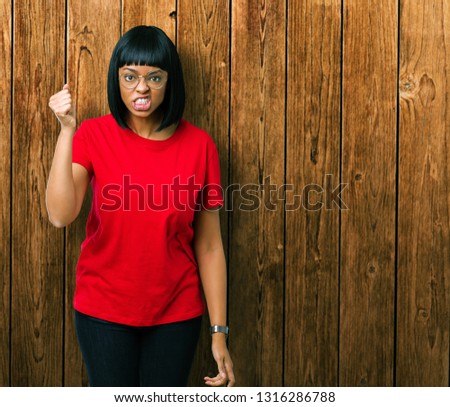 Beautiful young african american woman wearing glasses over isolated background angry and mad raising fist frustrated and furious while shouting with anger. Rage and aggressive concept.