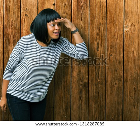 Beautiful young african american woman wearing stripes sweater over isolated background very happy and smiling looking far away with hand over head. Searching concept.
