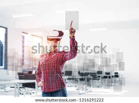 Woman in casual wearing virtual reality mask and touching icon on screen. Mixed media