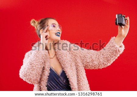 Time to smile. Young blonde-haired woman wearing pink fluffy coat smiling while making selfie
