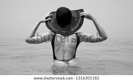 Back view of woman in the sea water. Girl wearing swimsuit and straw hat enjoying her holiday  - black and white photography