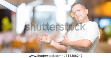 Middle age arab man wearig white t-shirt over isolated background Inviting to enter smiling natural with open hand