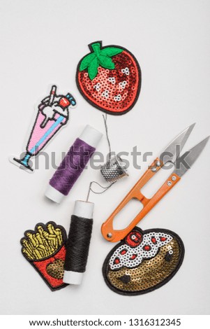Thread, thimble, scissors and decorative patches on white background. Custom design, sewing and repair of worn clothes.
