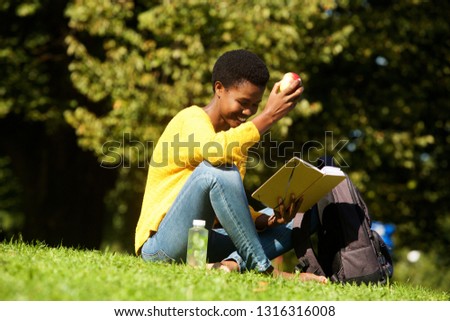 Portrait of young african american woman witting in park reading book