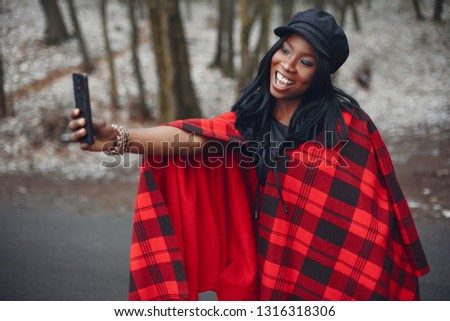 Beautiful black girl in a red shirt. Ethnic woman in a winter forest. Lady with mobile phone