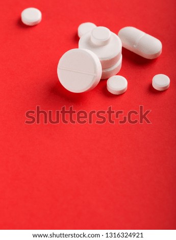 Assorted pharmaceutical medicine pills, tablets and capsules. Red background.