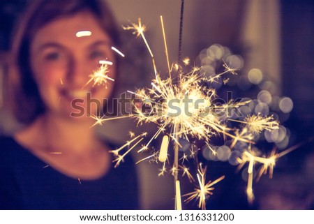 Smiling girl is holding a sparkler in her hand, indoor, lights in background