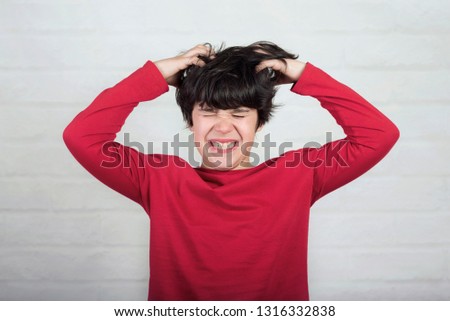 boy scratching his hair for head lice against brick background