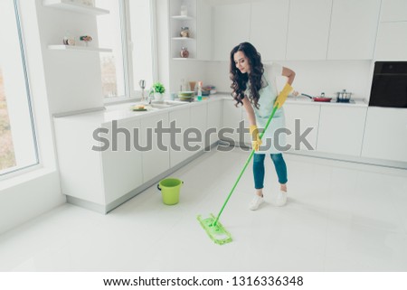 FUll length body size photo beautiful busy nice duties she her lady housewife wash white floor carefully not hurry housemaid wear jeans denim casual t-shirt covered by cute apron bright light kitchen