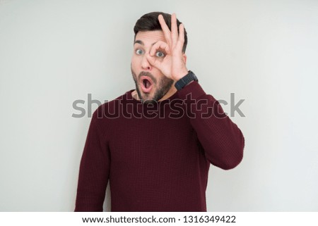 Young handsome man wearing a sweater over isolated background doing ok gesture shocked with surprised face, eye looking through fingers. Unbelieving expression.