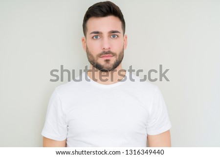Young handsome man wearing casual white t-shirt over isolated background with serious expression on face. Simple and natural looking at the camera.