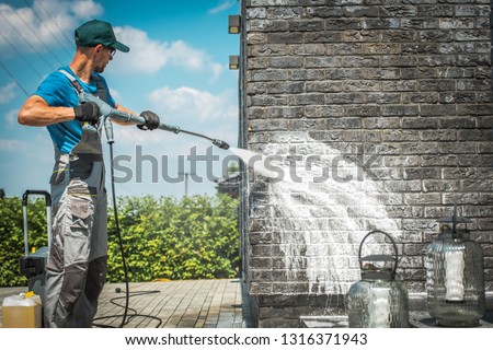 Brick House Wall Pressure Washing with Special Cleaning Detergent. Caucasian Men in His 30s. Taking Care of the Building Elevation. Royalty-Free Stock Photo #1316371943