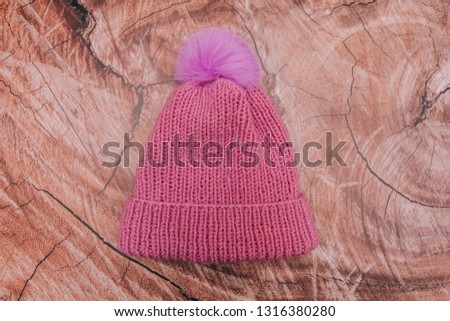 Warm knitted wool hat with a bubo of pink color on a wooden background