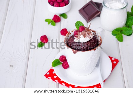 Chocolate mug cupcake with whipped cream, chocolate chips and fresh raspberries on a white wooden background.