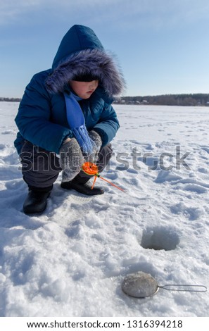 Boy fishing with a fishing rod on the ice in winter .