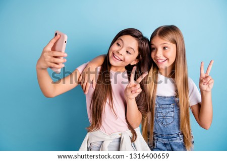 Close up photo two little she her blond brunette girls long pretty hair telephone make take selfies for mom mommy show v-sign wearing casual jeans denim t-shirts isolated blue bright background