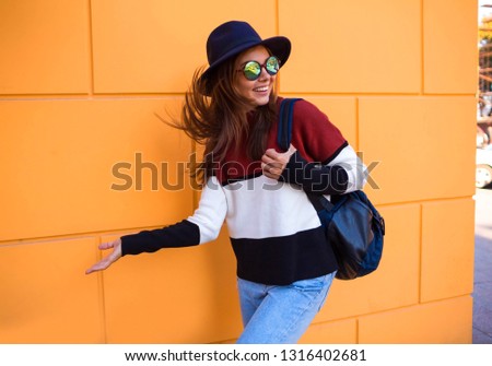 Image of joyful brunette woman walking against yellow wall outdoor and looking backward with silver laptop and takeaway coffee in hands.Cheerful woman in the street drinking morning coffee in sunshine