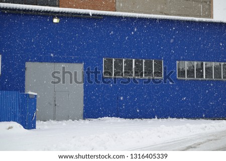 Snowfall on the background of an industrial warehouse of blue metal.