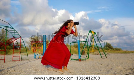 Beautiful girl taking picture on the sea beach in red dress