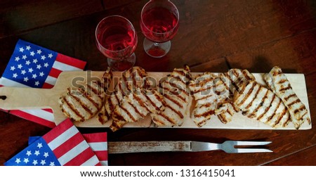 Fresh Grilled/BBQ Chicken, Top View, On Wooden Board, With Filled Wine Glasses and American Holiday Party Napkins to the Side on a Rustic Wood Background Royalty-Free Stock Photo #1316415041