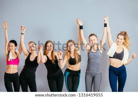 Group of six young sporty girls holding by hands while standing at grey wall in pilates studio. Female companions in gym resting after fitness, indoor.