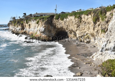 This picture of a sea cave on a warm sunny day is in the area of shell beach, California. Ocean waves and a sea cave with green plants surrounding it.