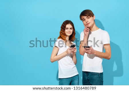 pretty man and woman stand next to the phones in their hands and communicate with each other on a blue isolated background