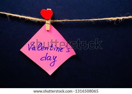 Pink  paper for notes  on the clothespin with hearts  on a dack blue background. Close up