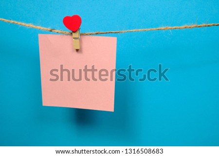 Pink  paper for notes  on the clothespin with hearts  on a blue background. Close up