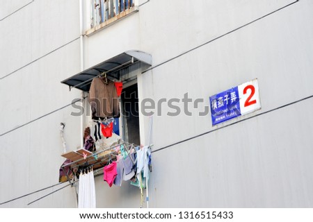 Laundry drying outside a window in a Chinese apartment building,with street sign at the facade of the building.Translation into English of the Chinese text written at the street sign