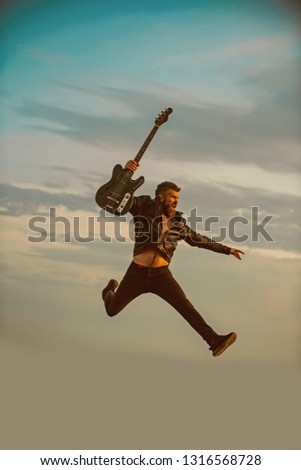 Freedom in his veins. Freedom, bearded man jump with guitar on blue sky.