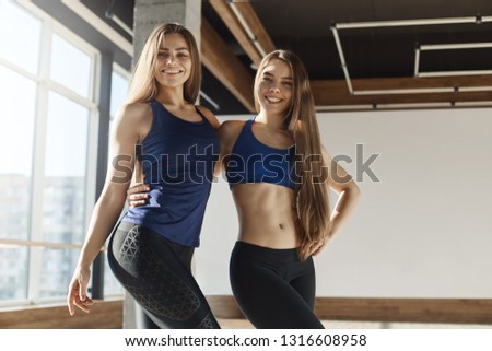 Two active and healthy female fitness instructors embracing gym class satisfied with good productive training session, girlfriends attending fitness together working-out for perfect body shape