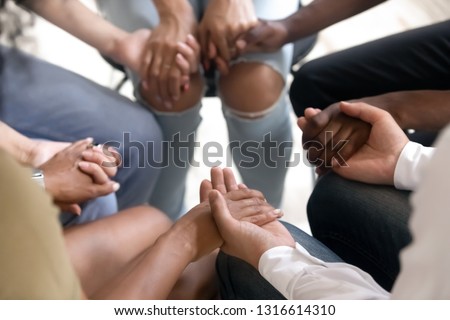 Diverse people sitting in circle holding hands at group therapy session, religious christian team pray together for recovery give psychological support, counseling training trust concept, close up Royalty-Free Stock Photo #1316614310