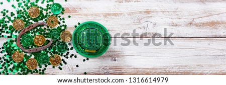 Bright green shamrock with gold coins, hat and rusty horseshoe for Saint Patrick Day on white rustic wooden background 