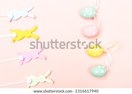 Easter background. Colorful bunnies shape cake toppers and painted eggs on pastel pink background. Flat-lay, top view. Copy space for your text.
