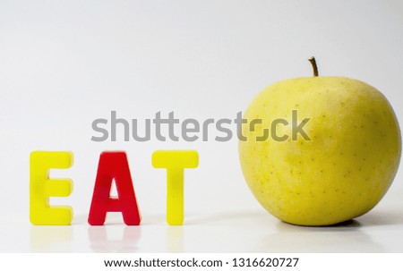 Green apple and the word eat written with plastic letters against a white background.